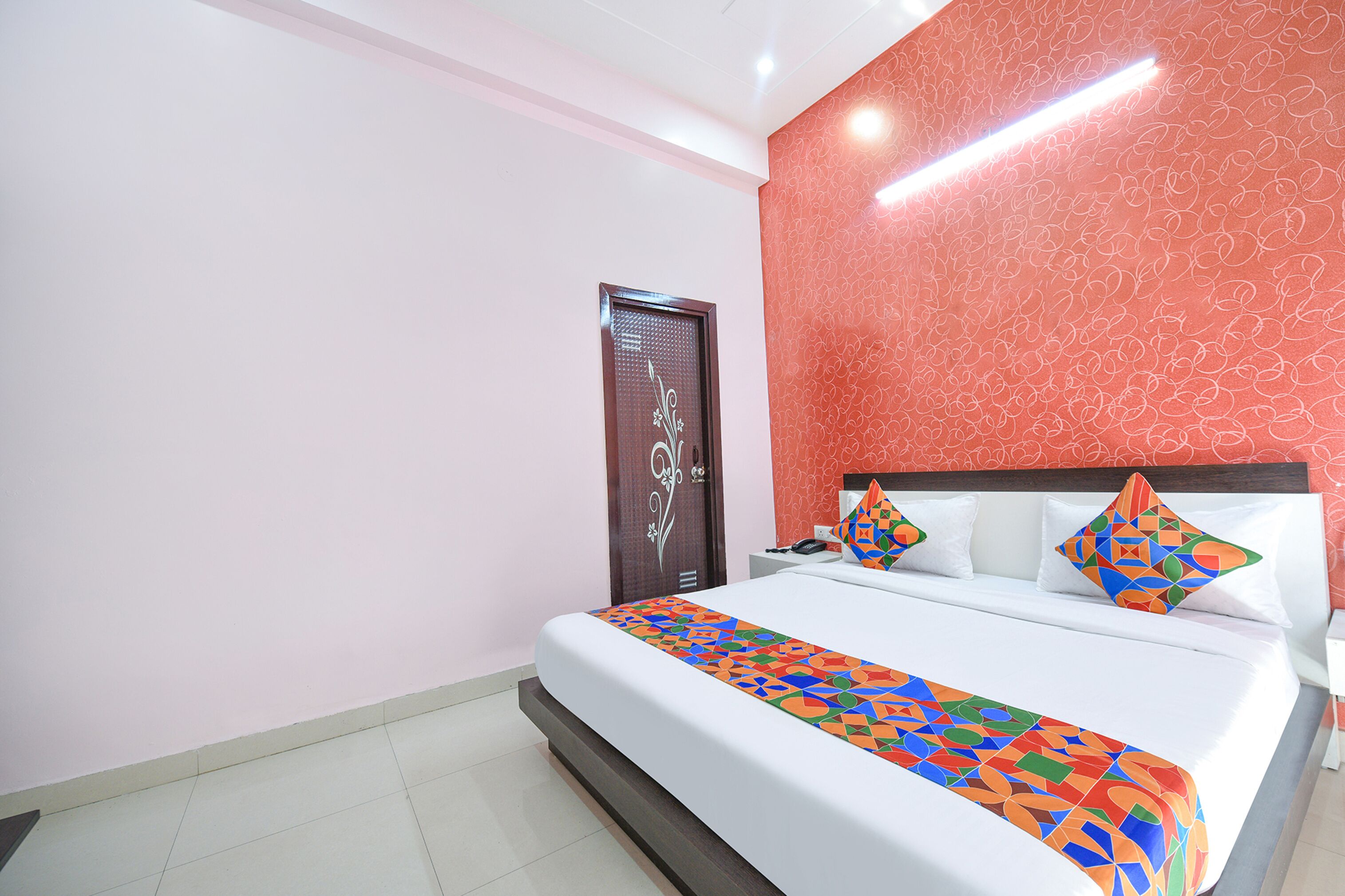 Un lit bien fait, avec une couverture aux motifs géométriques colorés, un oreiller blanc et une tête de lit décorative.