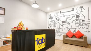 A reception desk with a 'fab hotels' sign, a sofa with red cushions, and a wall mural. - FabExpress Vivek (Prayagraj)