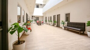A spacious corridor with a wooden floor, potted plants, a sofa, and doors leading to rooms. - FabExpress Vivek (Prayagraj)