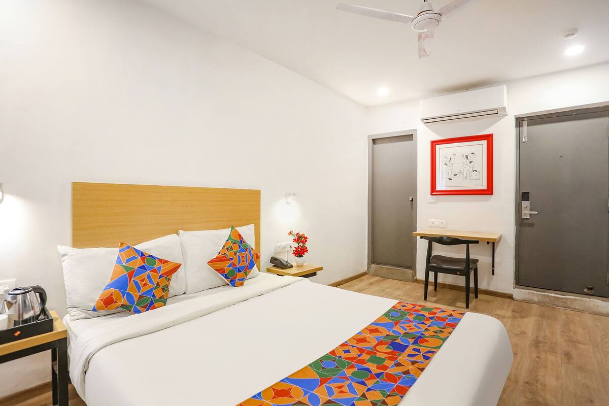 A hotel room with a bed, a desk, a chair, a nightstand, a lamp, and a framed picture on the wall.