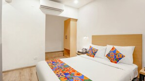 A hotel room with a bed, a nightstand, an air conditioning unit, and a wooden headboard. - FabExpress Vivek (Prayagraj)