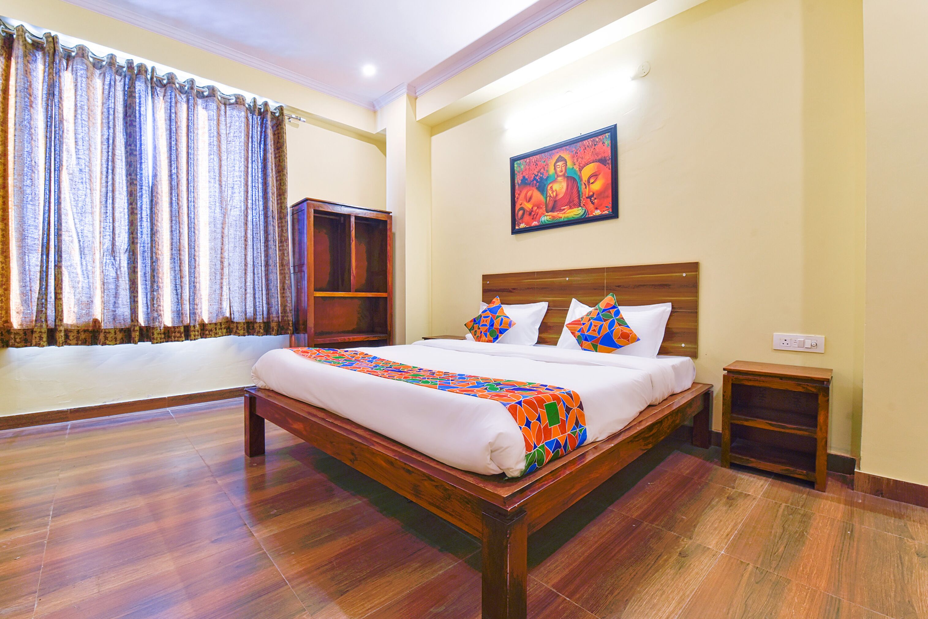 Una habitación de hotel con una cama de madera, almohadas coloridas, una mesita de noche pequeña y un cuadro en la pared.