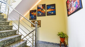 A staircase with granite steps and metal railings, leading to a landing with three abstract paintings and a potted plant. - Fabhotel Golden Manor Inn (Jaipur)