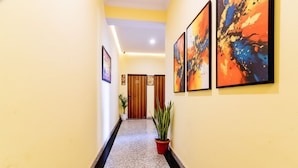 A hallway with a yellow wall, a black and white patterned floor, and three framed abstract paintings. - Fabhotel Golden Manor Inn (Jaipur)
