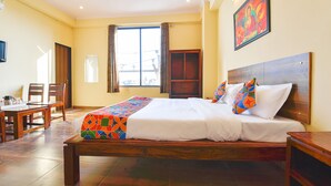A hotel room with a bed, a dining table, chairs, a window with curtains, and a painting on the wall. - Fabhotel Golden Manor Inn (Jaipur)