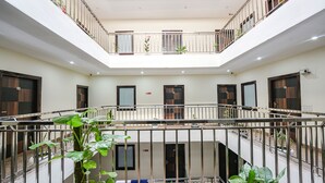 Ein mehrgeschossiges Atrium mit einer zentralen Treppe, Balkonen mit Geländern und Topfpflanzen.