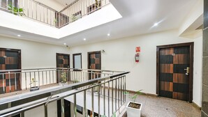 Ein mehrgeschossiges Innenraum mit einer zentralen Treppe, Blumentöpfen und einem Feuerlöscher an der Wand.
