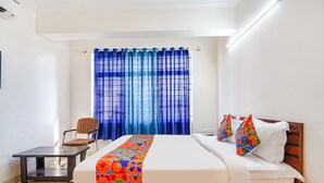 A neatly made bed with a colorful geometric-patterned bedspread, a wooden headboard, and two decorative pillows. A chair is positioned at the foot of the bed, and a small table is beside it. - Fabhotel Emirates Inn (Bengaluru)