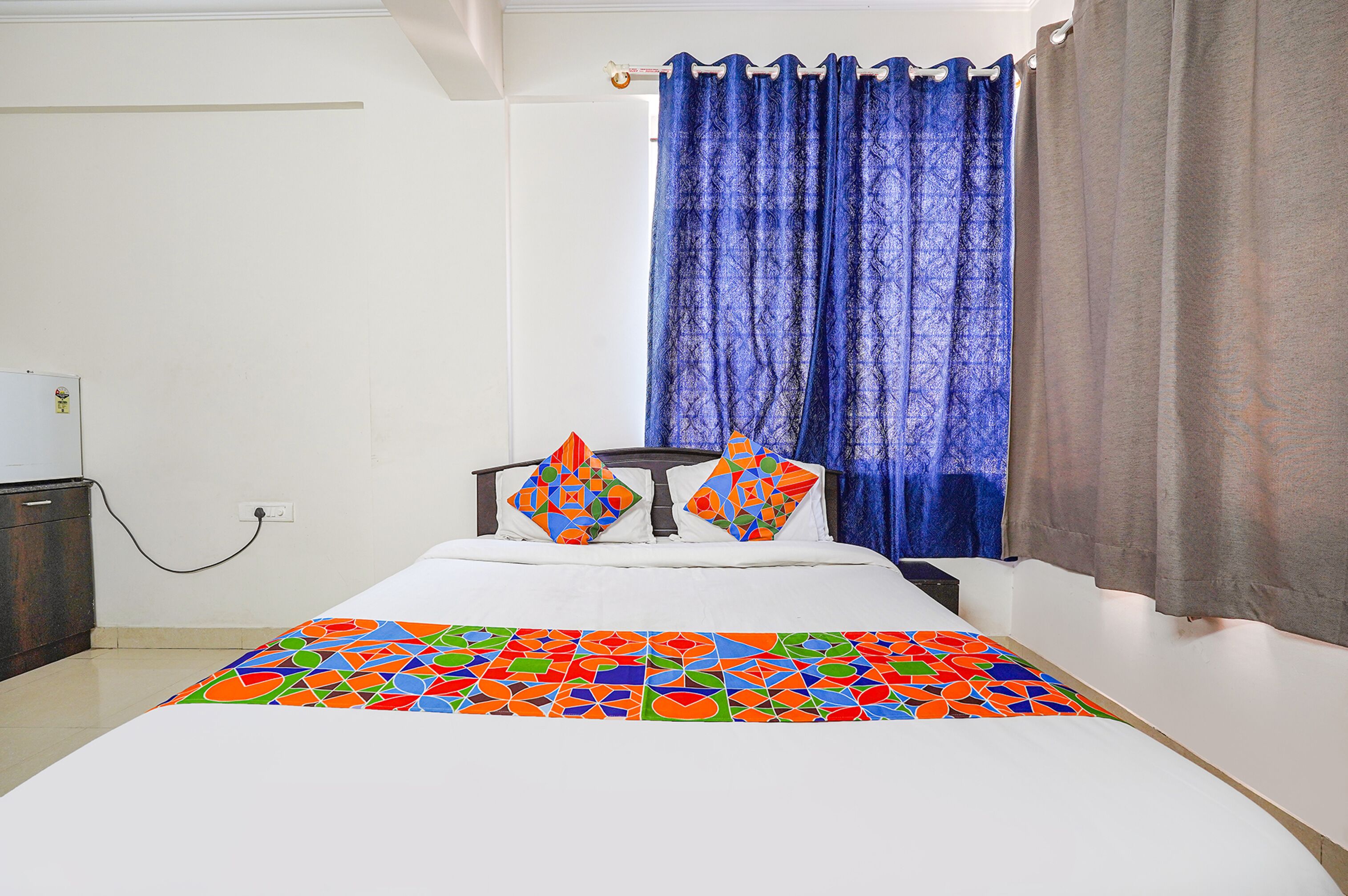 A bed with colorful bedding, a dark headboard, and a window with blue curtains.