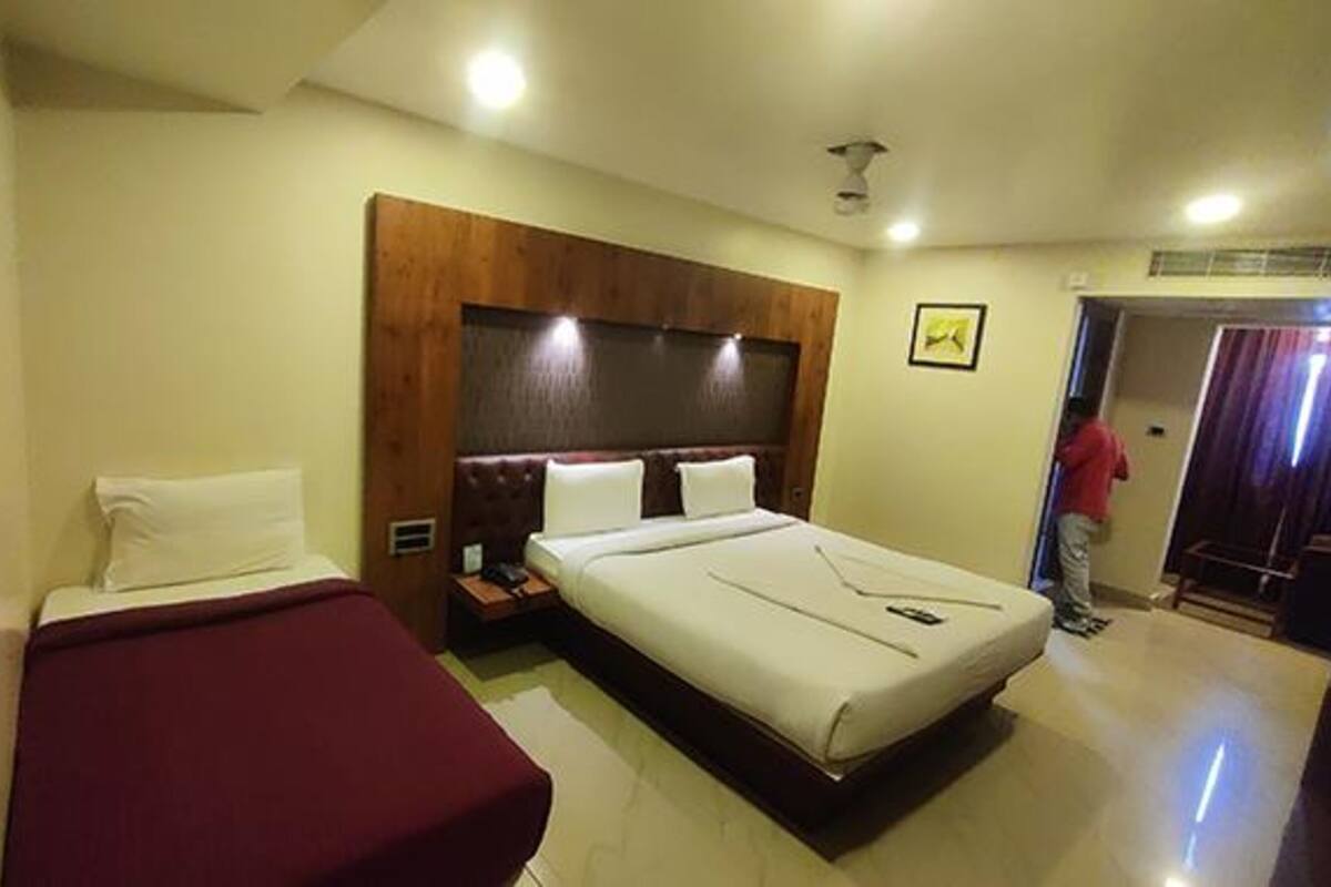 A hotel room with a large bed, a smaller bed, a wooden headboard, a nightstand, and a door.