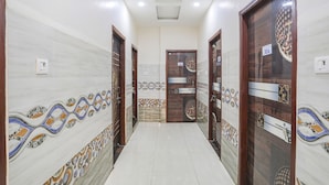 A hallway with patterned walls, a tiled floor, and wooden doors with numbered plaques. - Fabexpress Convivial Star (Raipur)