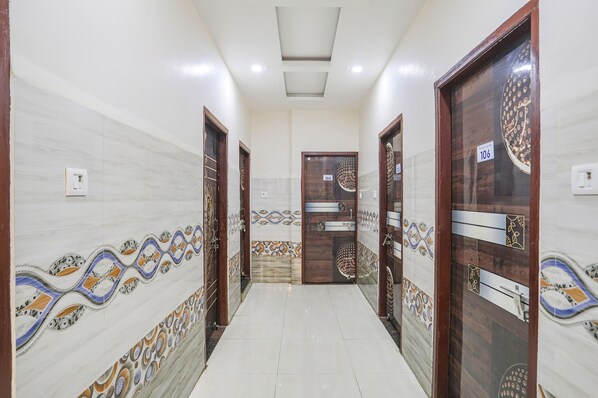 Un pasillo con paredes estampadas, piso de baldosas y puertas de madera con placas numeradas.