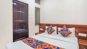 A hotel room with a wooden door, a window, a bed with colorful bedding, and a bedside table. - Fabexpress Convivial Star (Raipur)