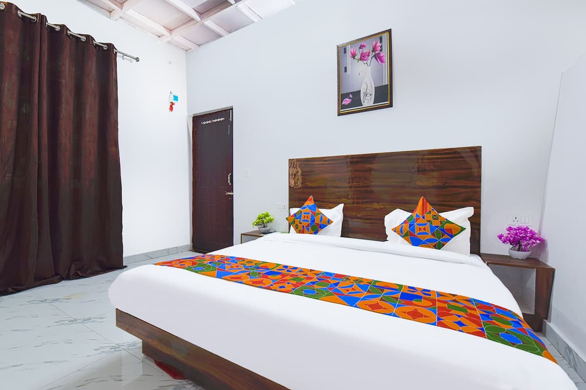 A hotel room with a large bed, a wooden headboard, a nightstand with a vase of flowers, and a door with a sign.