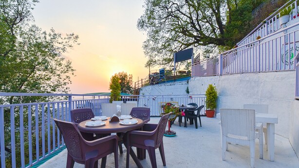 Eine Terrasse im Freien mit einem runden Tisch und Stühlen, umgeben von einem weißen Zaun und Blumentöpfen.