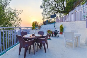 Une terrasse extérieure avec une table ronde et des chaises, entourée d’une clôture blanche et de plantes en pot.