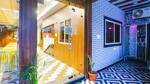 A hotel lobby with a wooden reception desk, a reception area, and a blue brick wall with a window. - Fabhotel Prime Diamond Palace (Bhopal)