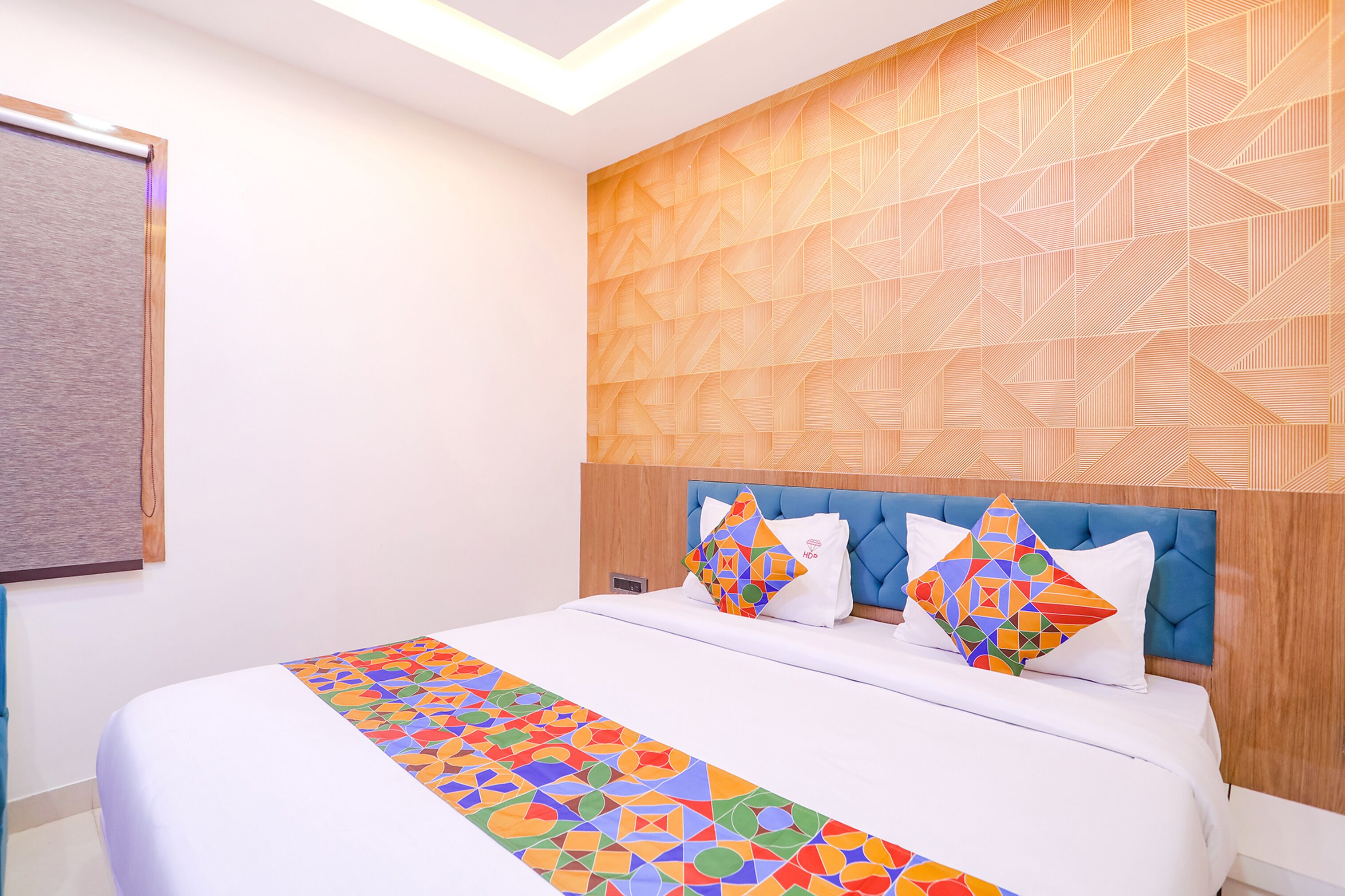 A neatly made bed with a colorful geometric-patterned bedspread, a blue upholstered headboard, and two decorative pillows with geometric patterns.
