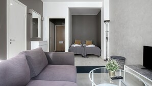 A modern hotel room with a grey sofa, a bed with two pillows, a TV, and a small side table with a plant. - Kotimaailma Aparthotel Kamppi - Studios (Helsinki)