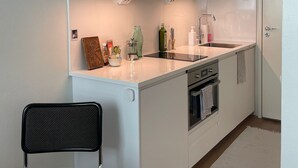 A compact kitchen with white cabinets, a countertop, a sink, and a stove. There is a chair and a small table in the foreground. - Kotimaailma Aparthotel Kamppi - Studios (Helsinki)