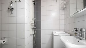 A modern bathroom with white tiles, a sink, a toilet, a shower, and a towel rack. - Kotimaailma Aparthotel Kamppi - Studios (Helsinki)