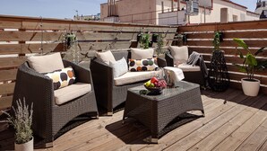 A rooftop patio with wicker furniture, potted plants, and a fruit bowl.