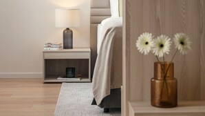 A modern bedroom with a bed, bedside table, lamp, and a vase with flowers.