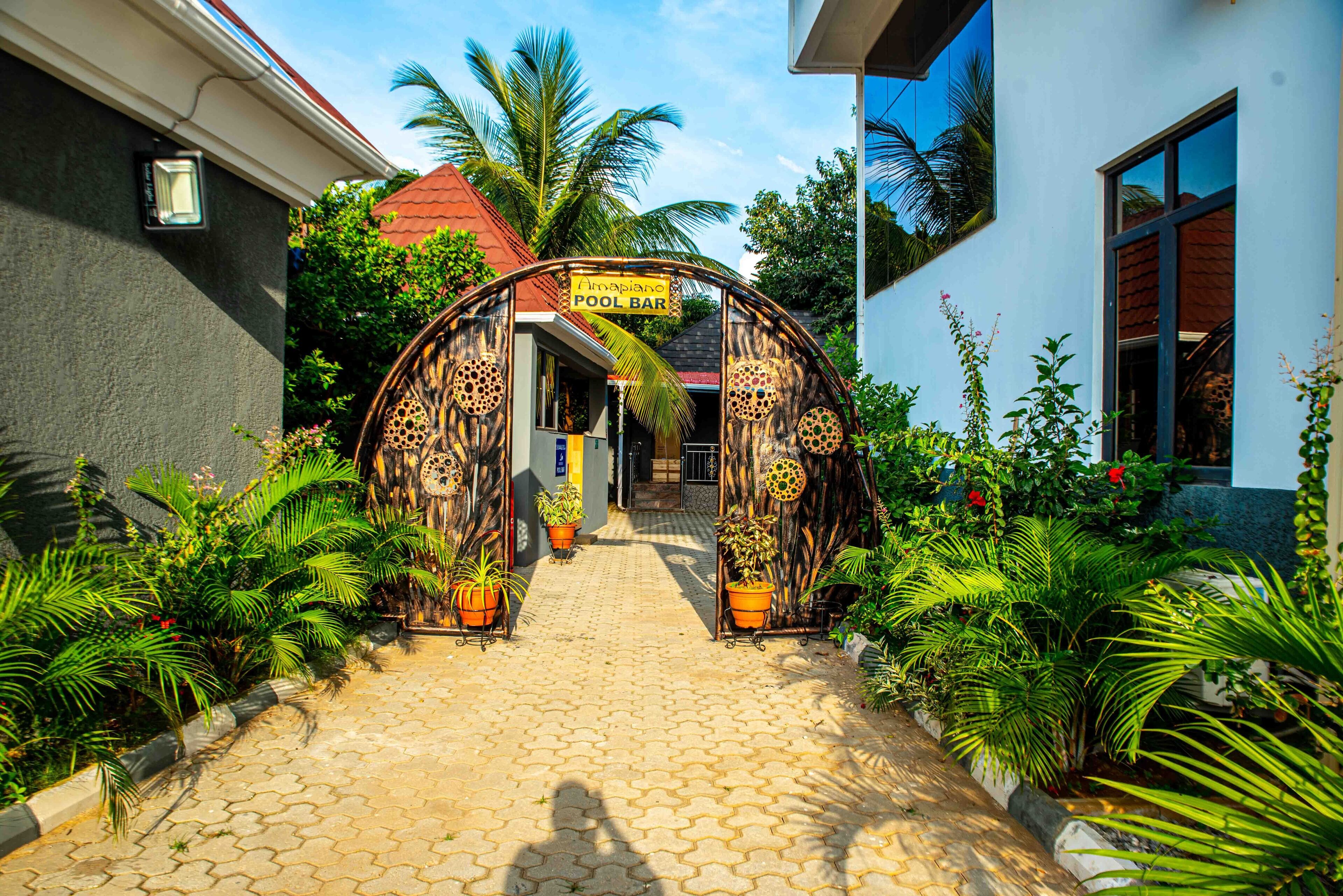 A pathway leading to a pool bar with a tropical archway, surrounded by potted plants and palm trees.