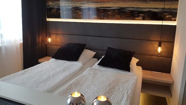 A hotel room with a bed, two bedside tables, and a wall-mounted painting of a sunset over the ocean. - Kleine Düne (Cuxhaven)