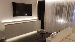 A modern living room with a flat-screen TV mounted on the wall, a sofa, a small round table, and a decorative light fixture. - Kleine Düne (Cuxhaven)