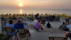 A sunset view from a terrace with yellow chairs and tables, overlooking the sea. - Kleine Düne (Cuxhaven)