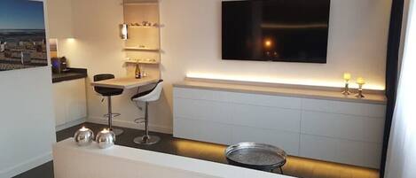 Ett hotellrum med en säng, ett skrivbord med en stol, en tv som är monterad på väggen och ett litet bord med en lampa.