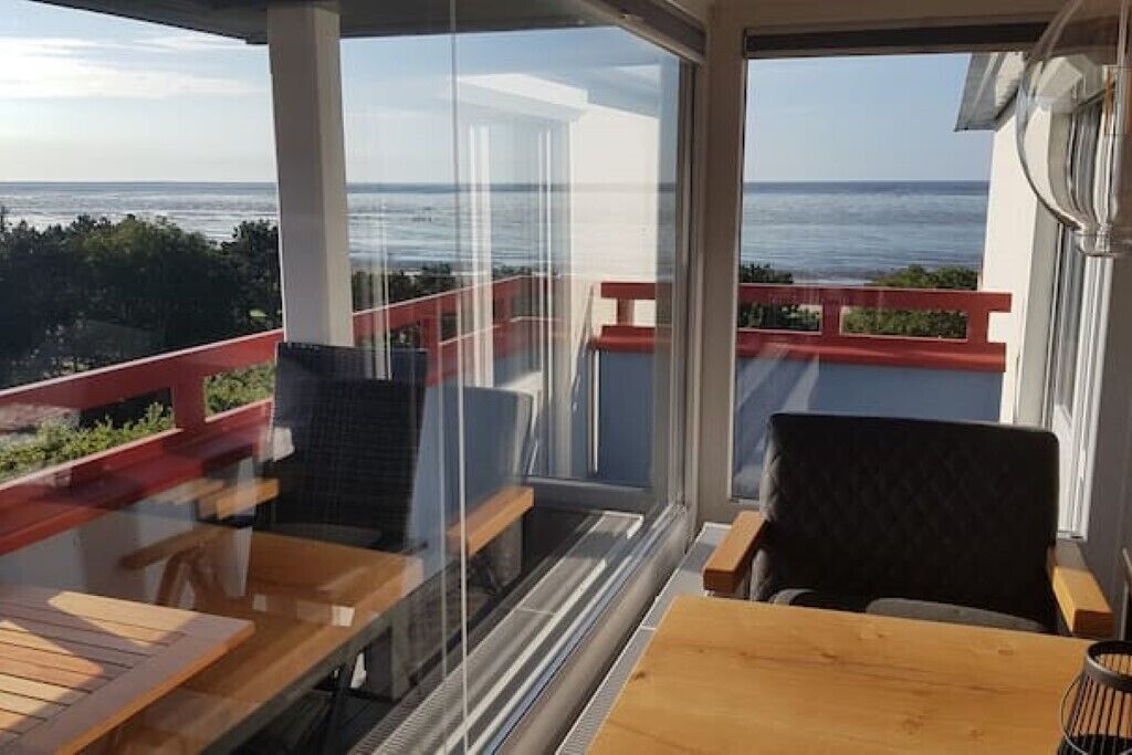 Un balcon avec vue sur la mer, des meubles en bois et une cloison en verre.