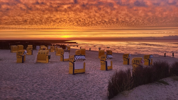 A beach with numbered beach chairs and umbrellas, a clear sky, and a sunset over the ocean. - Little Skysuite W 94 (Cuxhaven)