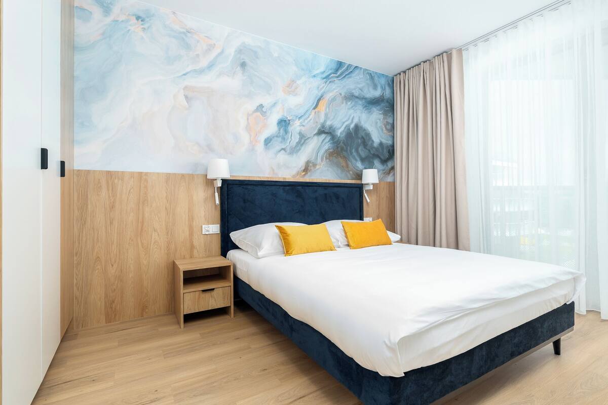 Un dormitorio moderno con una cama grande, una mesita de noche de madera y una pared de mármol.