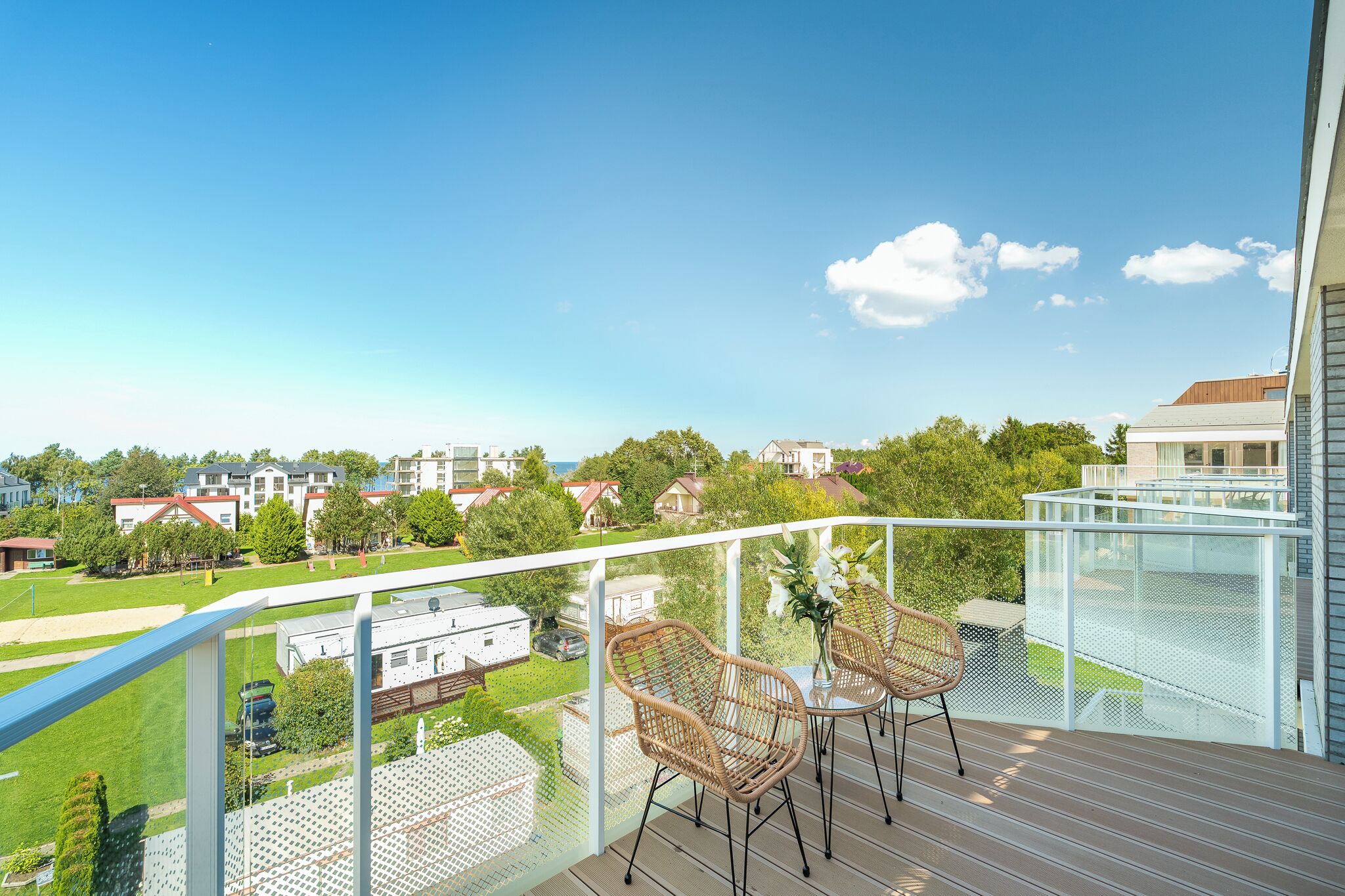 Un balcon doté de fauteuils et d’une table en osier, offrant une vue sur un quartier résidentiel avec ses maisons et sa verdure.