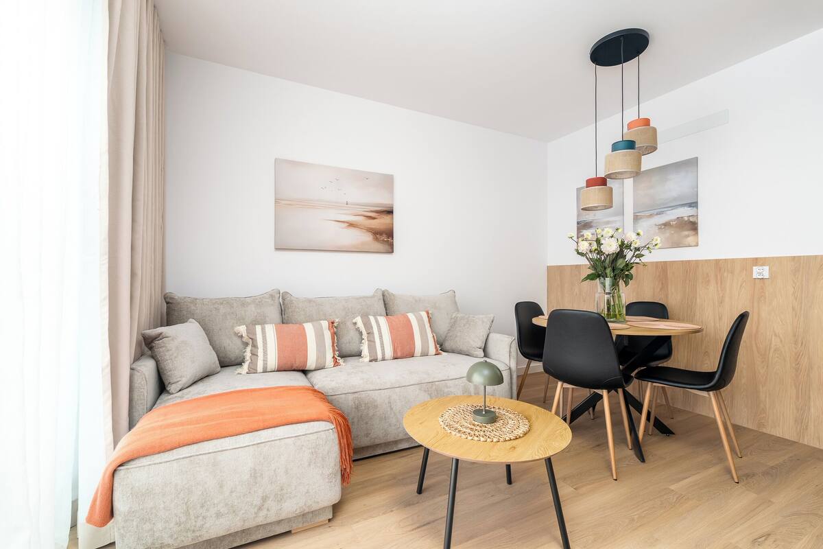 Una sala de estar moderna con un sofá gris, una mesa redonda de madera, sillas negras y una lámpara colgante.