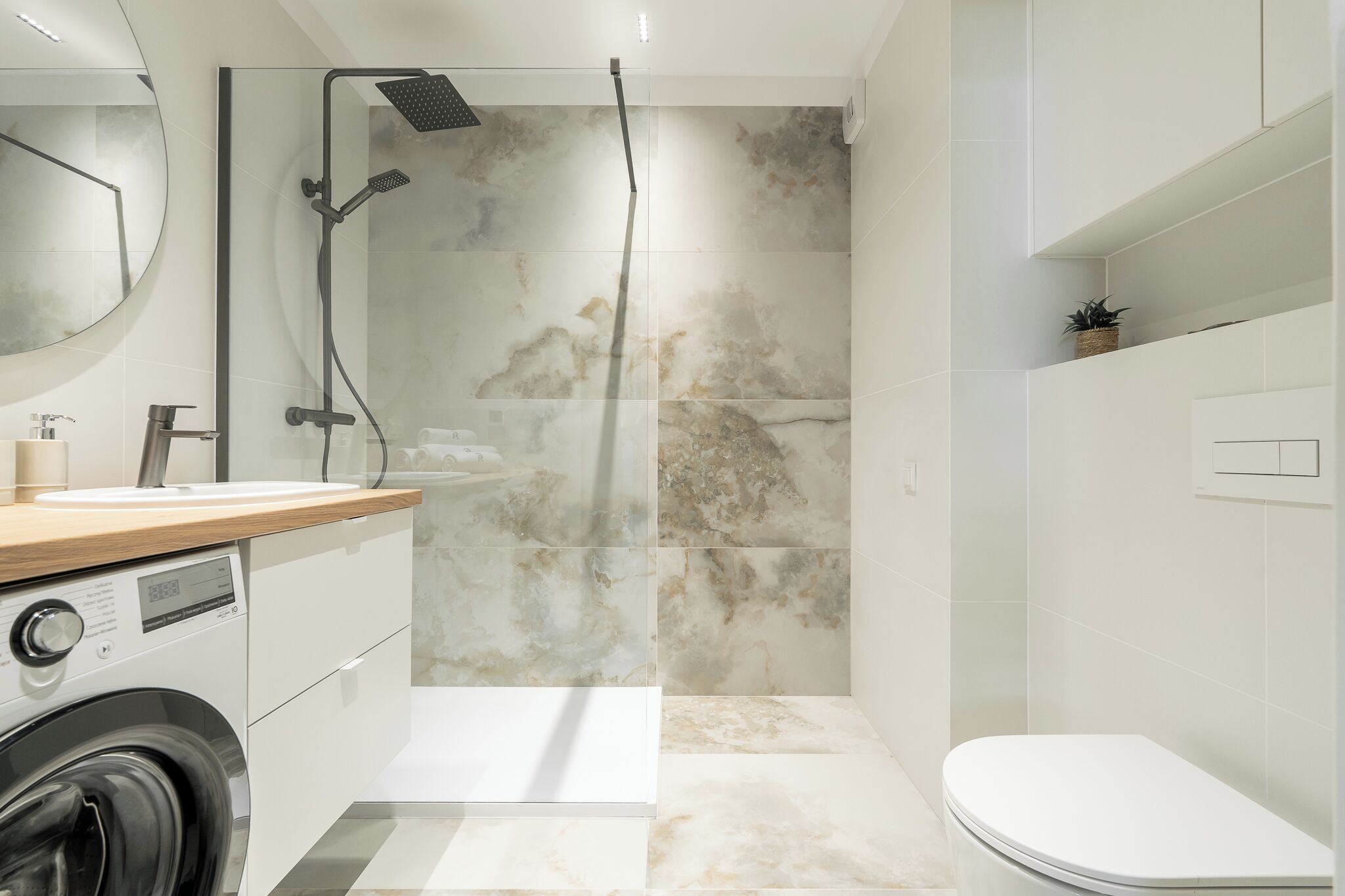 Et moderne badeværelse med bruseniche, indbygget vaskemaskine og toilet.