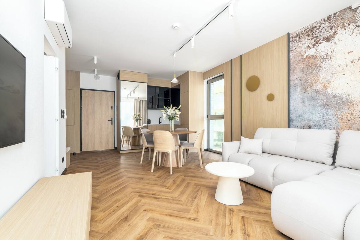 Una sala de estar moderna con un sofá, una mesa de comedor con sillas, y una cocina visible a través de una puerta abierta.