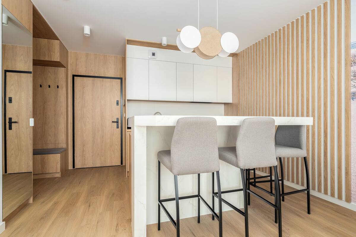 Una cocina moderna con armarios de madera, encimera blanca y dos taburetes grises.