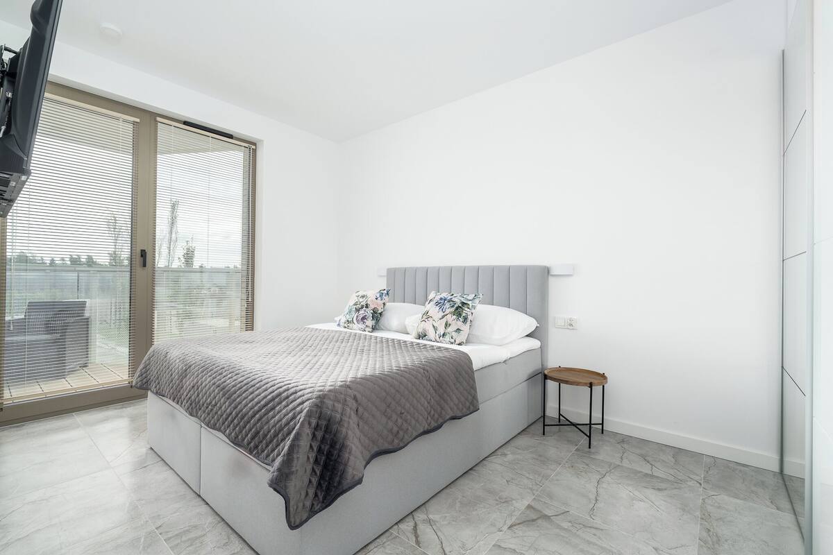 Un dormitorio moderno con una cama grande, una mesita auxiliar pequeña y vistas a través de un ventanal corredero.