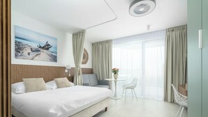 Une chambre d’hôtel moderne avec un grand lit, une petite table avec une chaise, une fenêtre ronde et un tableau au mur.