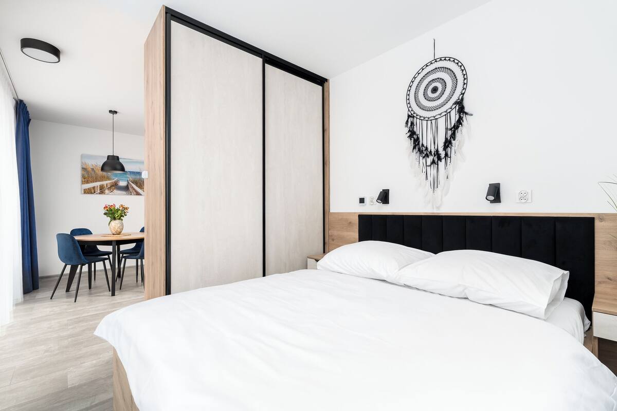 Un dormitorio moderno con cama, un escritorio y sillas, y un atrapasueños colgado en la pared.