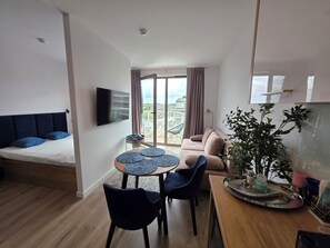 Una sala de estar moderna con sofá, una mesa de comedor con sillas, televisor montado en la pared y un balcón con vistas.