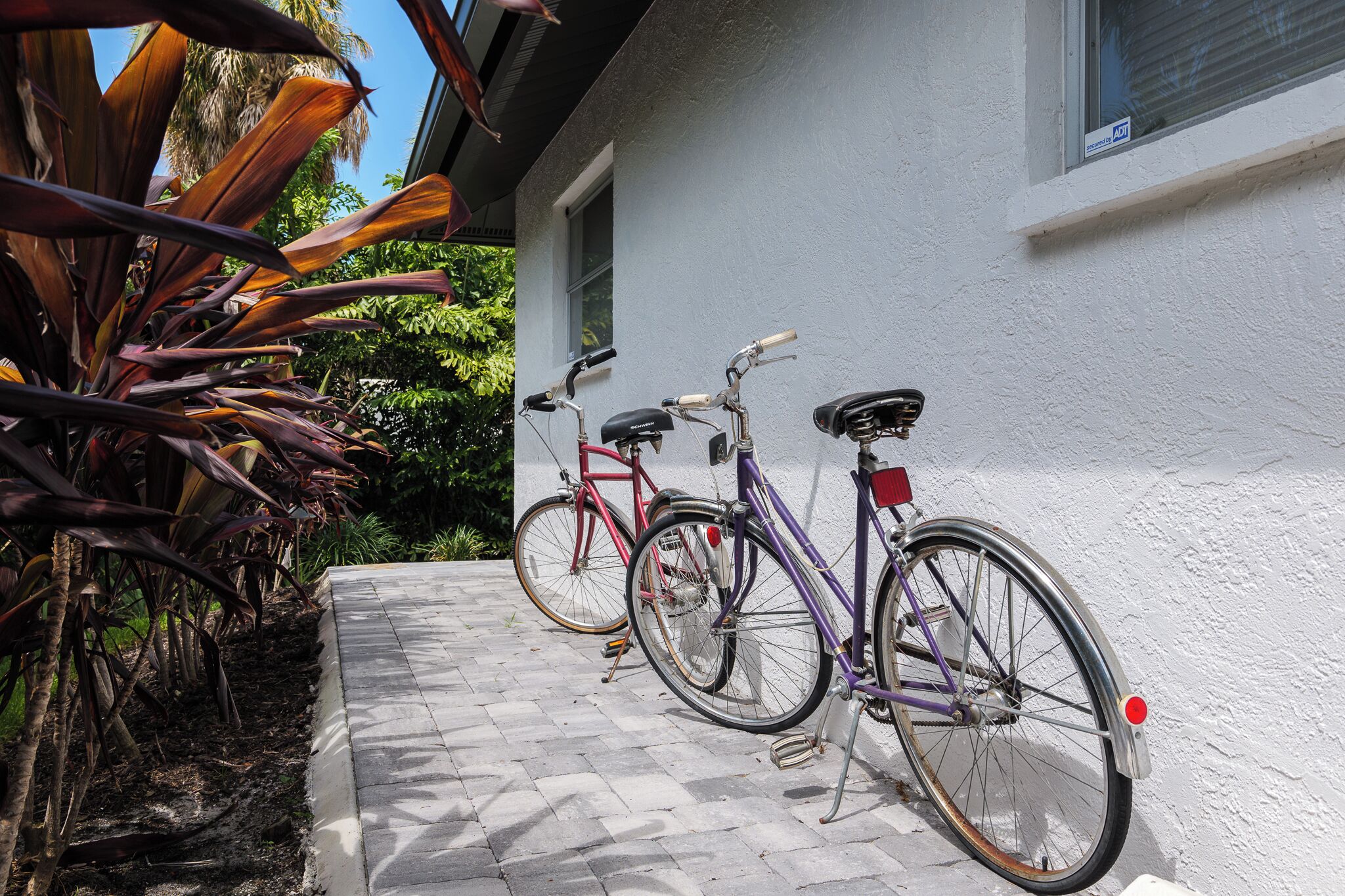 A paved pathway leading to a white building with two bicycles parked against it.