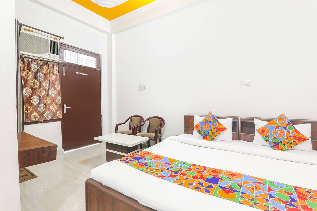 Habitación de hotel con cama, escritorio, dos sillas, armario y aire acondicionado.