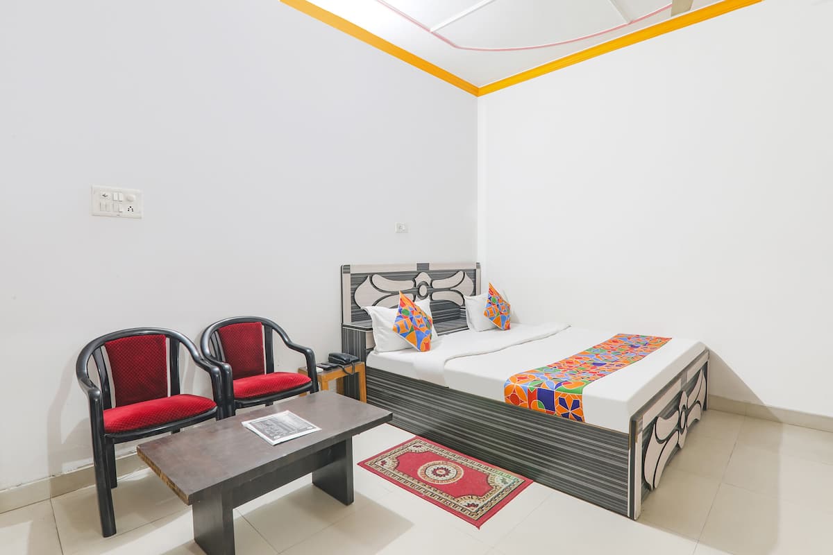 Una habitación pequeña y limpia con una cama, dos sillas, una mesa y una alfombra roja.