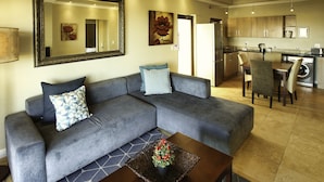 A modern living room with a grey sectional sofa, a coffee table with a decorative basket, and a dining area with a table and chairs. - Ellefsen Golf Suite 106 Langebaan 4-slpr (Langebaan)