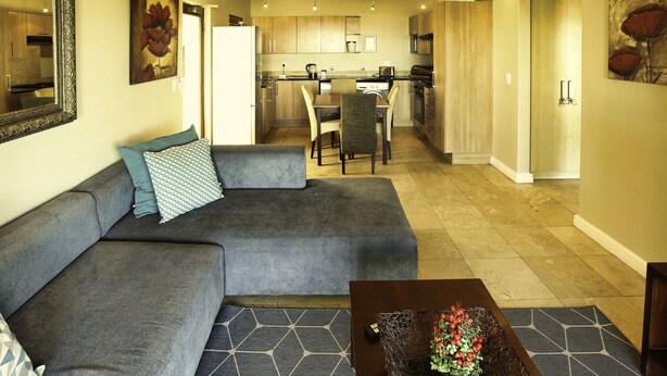 A modern living room with a gray sectional sofa, a coffee table with a vase of flowers, and a dining area with a table and chairs. - Ellefsen Golf Suite 106 Langebaan 4-slpr (Langebaan)