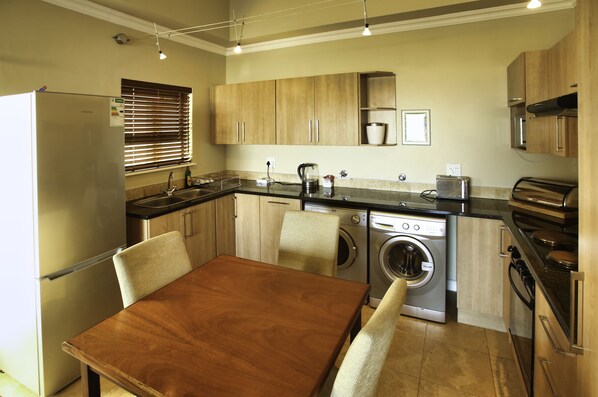 A compact kitchen with a dining area, including a refrigerator, sink, stove, and washing machine.